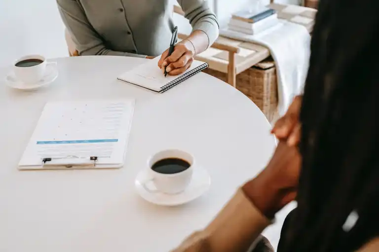 Two people talking over coffee and notes at a bright table
