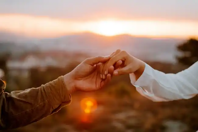 Two people holding hands gently at sunset